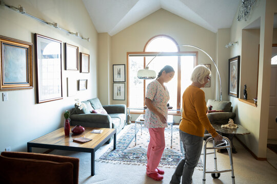 Home caregiver with senior woman using walker in living room