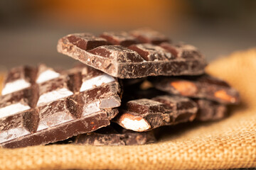 Broken chocolate pieces on wooden background. Selective focus.