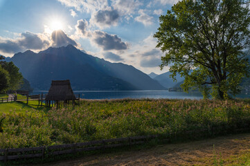 Summer on Lake Idro, view of the archaeological area of the museum of stilts on the lake. Bronze age. Light reflections on water, sun ray in the clouds.  Trentino Alto Adige near Garda Lake, Italy.