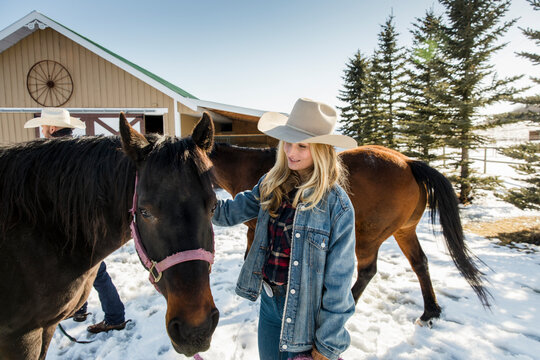 Female rancher with horse in snow outside winter barn