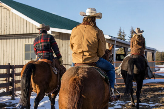 Ranchers horseback riding outside sunny winter barn