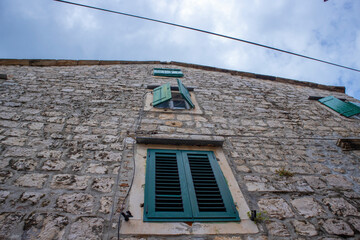 Beautiful dalmatian stone house, traditional piece of architecture with green shutters, against cloudy sky