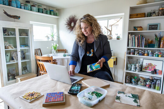 Female Artist With Mosaics Working At Laptop In Home Art Studio