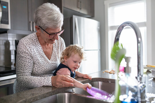 Grandmother and toddler granddaughter doing dishes at kitchen sink