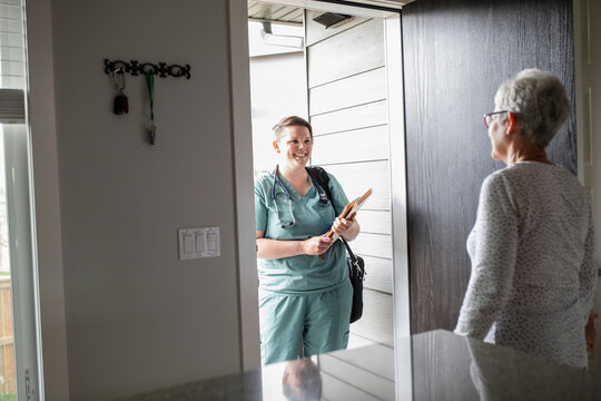 Senior woman greeting home caregiver nurse at front door