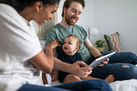 Happy couple with baby son using digital tablet on bed