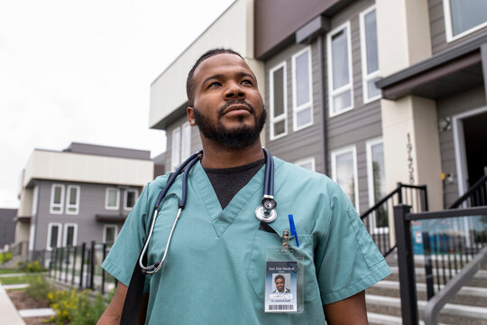 Male home caregiver in scrubs outside townhouse