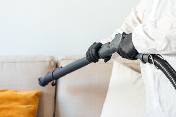 Detail of a tube from a disinfection machine that is held by a man with PPE disinfecting the living...
