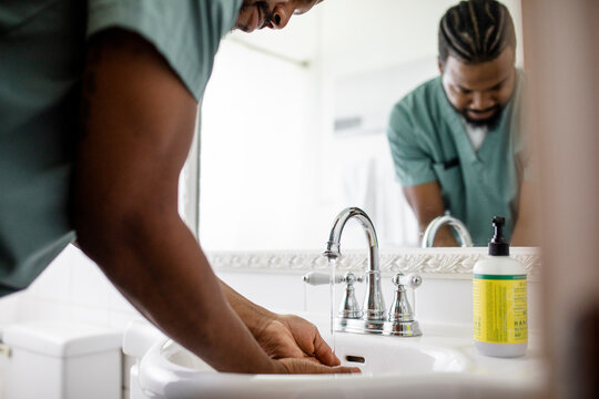 Male nurse washing hands at bathroom sink