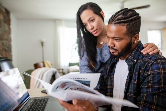 Couple Reading Paperwork At Laptop