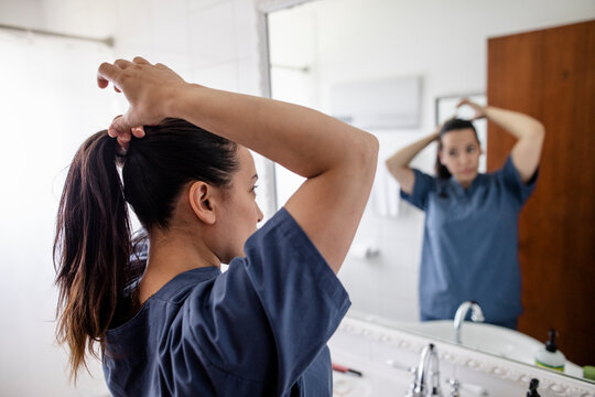 Female nurse fixing hair into ponytail at bathroom mirror