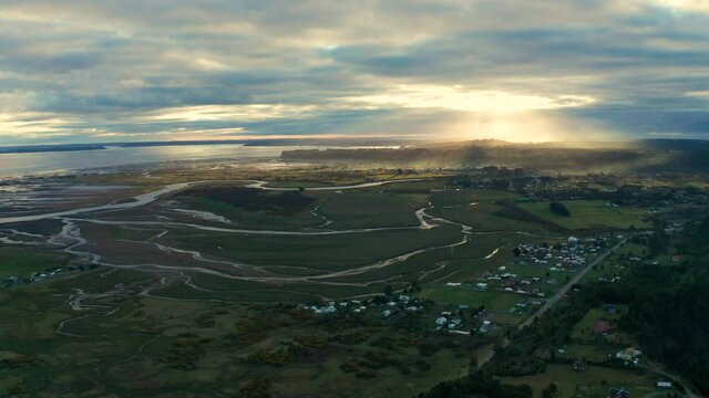 aerial view of wetlands and delta of the Chamiza river at its mouth to the bosom of Reloncavi, in a cloudy sunset with sun rays crossing the clouds