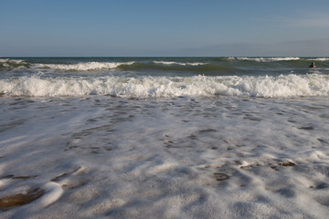 Sandy seashore, foamy oncoming waves and a beautiful sky on a summer sunny day.
