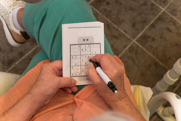 Persona mayor ejercitando el cerebro haciendo un sudoku.  - obrazy, fototapety, plakaty