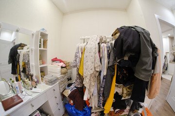 A room cluttered with clothes and a female dressing table with cosmetics, no closet