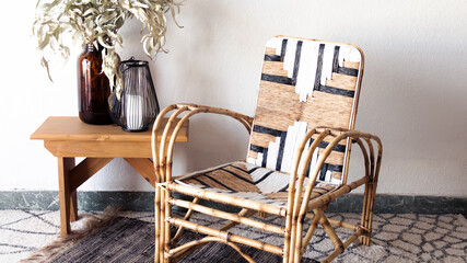 Sillón de mimbre y caña reciclado y pintado con un moderno patrón geométrico aislado dentro de una habitación blanca e iluminada junto a elementos decorativos para hacer más confortable el ambiente. 