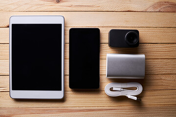 group of portable information devices on a wooden rustic desk. white tablet, silver power bank, smartphone and action video camera. blogger hardware setup