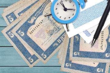 5 Ukrainian hryvnias bills and alarm clock with pen and envelopes. Tax season concept, payment deadline for credit or loan. Financial operations using postal service