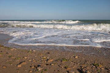 Fototapeta na wymiar Sandy seashore, foamy oncoming waves and a beautiful sky on a summer sunny day.