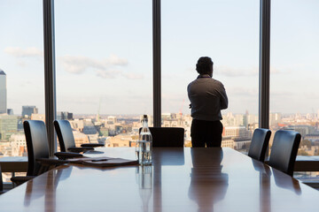Thoughtful businessman looking out urban conference room window
