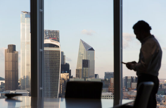 Businessman using smart phone at highrise office window, London, UK