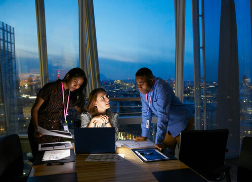 Business people working late at laptop in highrise conference room
