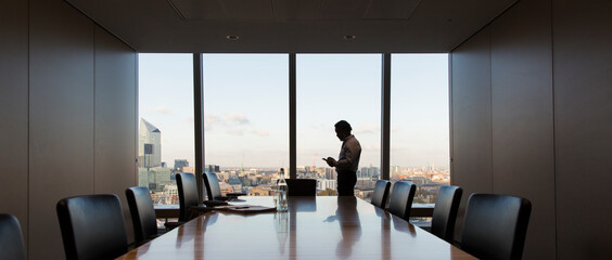 Businessman using smart phone at highrise conference room window