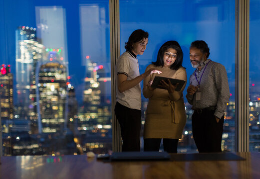 Business people with digital tablet working late at window, London, UK