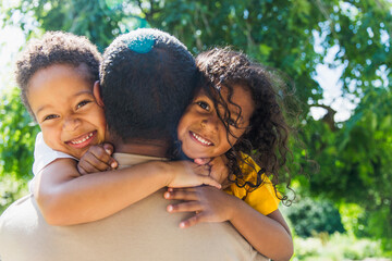 Happy daughter and son hugging father in sunny park