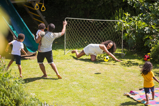 Happy family playing soccer in sunny summer backyard
