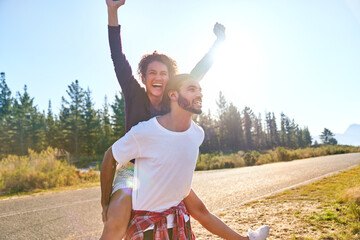 Portrait carefree young couple piggybacking at sunny remote roadside