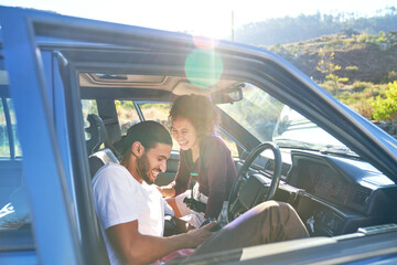 Happy young couple laughing on road trip in sunny car