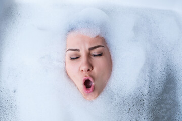 Closeup portrait of a girl in a bathtub and white foam around her face. Different emotions, grimaces, woman smile