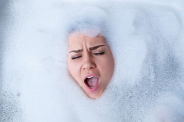 Fototapeta premium Closeup portrait of a girl in a bathtub and white foam around her face. Different emotions, grimaces, woman smile