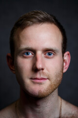 Fototapeta premium Young man shaving his beard. He shaved off half the bristles against a gray background. Male face care. Shaving bristles. The difference between skin without hair and with a mustache