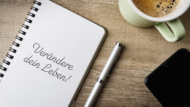 Ver&auml;ndere dein Leben! Flat Lay. Arbeitsbereich mit Notizblock, Kugelschreiber, Handy und einer Tasse Kaffee.