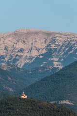 Fototapeta na wymiar Pequeña capilla aislada en una cima frente a la imponente cordillera montañosa de los Pirineos en la provincia española de Lérida.