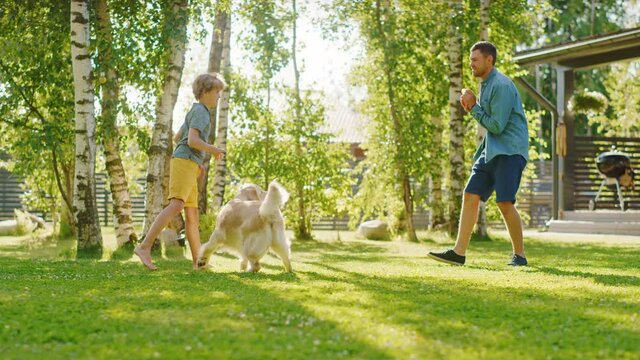 Handsome Father, and Son Play Catch With Loyal Family Friend Golden Retriever Dog. Family Spending Time Together Training Dog. Sunny Day Idyllic Suburban Home Backyard. Slow Motion Shot