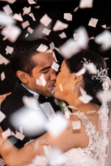 Latino Bride and Groom kissing with white confetti flying around them