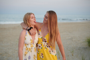 Two beautiful blonde sisters laugh as they pose together for family photo on the beach one...