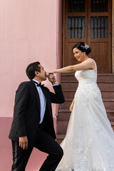 Latino Bride and Groom on door step while groom kisses her hand