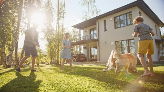 Smiling Beautiful Family of Four Play Catch flying disc with Happy Golden Retriever Dog on the Backyard Lawn. Idyllic Family Has Fun with Loyal Pedigree Dog Outdoors in Summer House. Handheld Low Shot