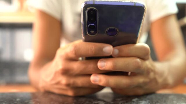 hands using blue mobile phone. Teenager using the mobile. Hands of dark man using a cell phone with black table and unfocused background. traveling of hands using the phone