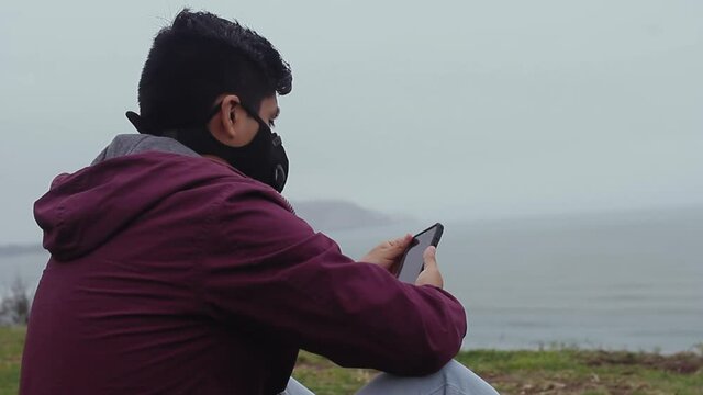 Un joven descansa con mascarilla por el parque mientras toma fotos durante la pandemia