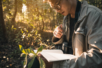 Botanists are taking note of the plants found in the tropical forests. Biologist researching in the forest. Botanist studying a newly flowering plant species. - obrazy, fototapety, plakaty