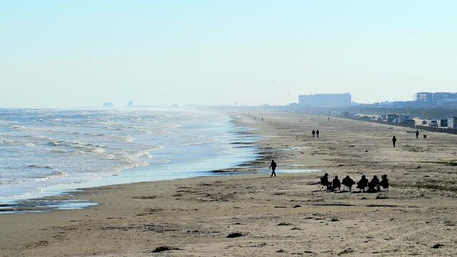 Afternoon beach scene at the Gulf of Mexico with sand, waves, cars and people enjoying themselves on a sunny day.
