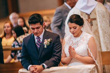 Latino bride and groom praying on their knees