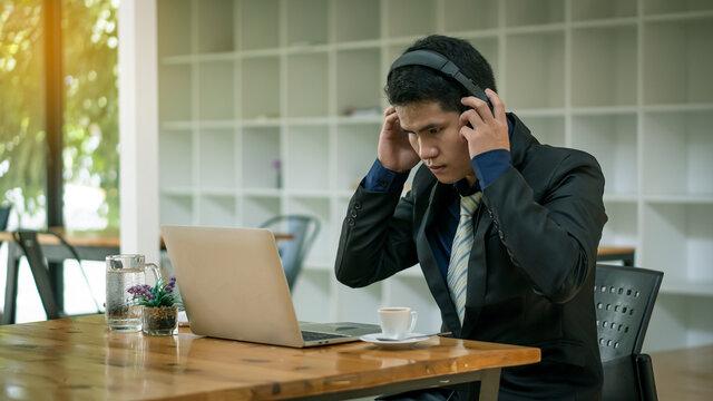 A young Asian businessman who works in front of a laptop listening to music with headphones in his hand.