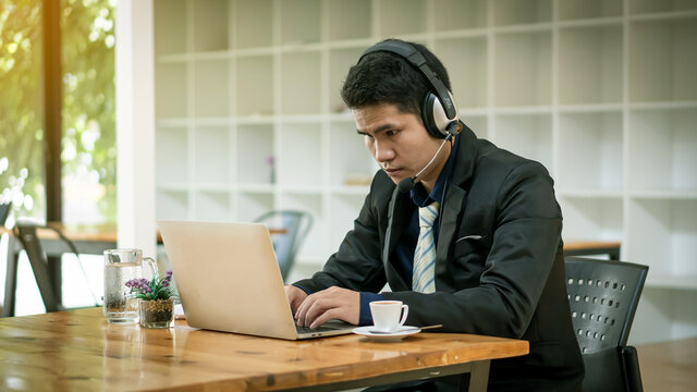 A young Asian businessman who works in front of a laptop listening to music in his office.