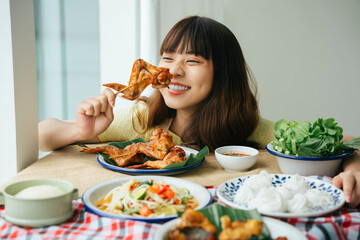 Portrait of young asian woman enjoy eating grilled chicken wing stick.